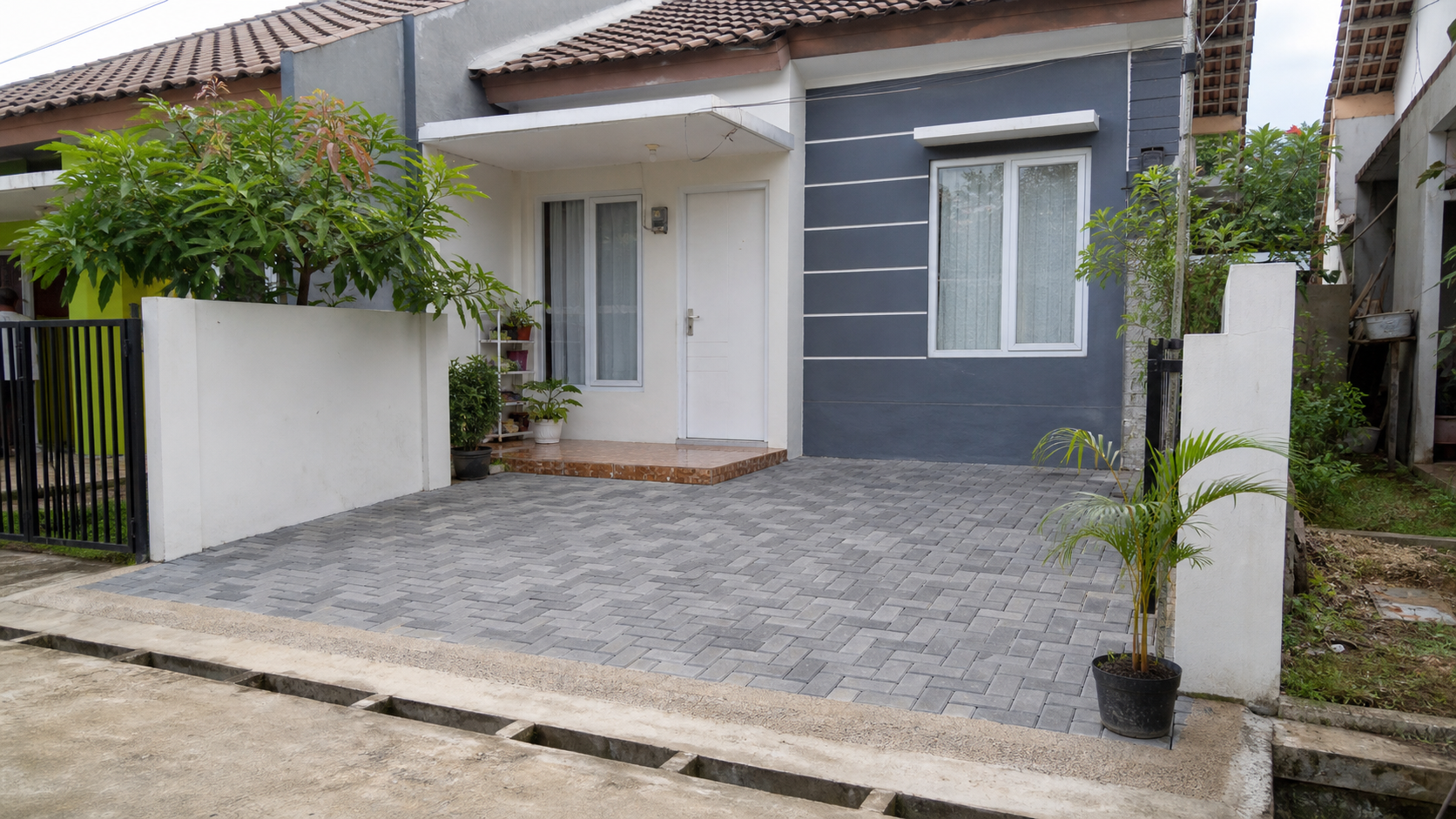 Rumah subsidi 1 lantai dengan halaman depan dan carport kecil memakai paving block abu-abu rapi